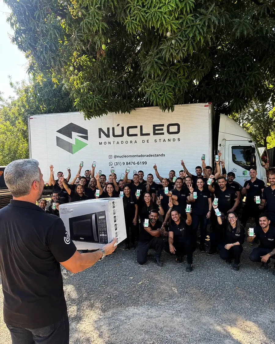 Equipe da Núcleo Montadora de Stands comemora com o app aberto enquanto o gestor entrega um micro-ondas